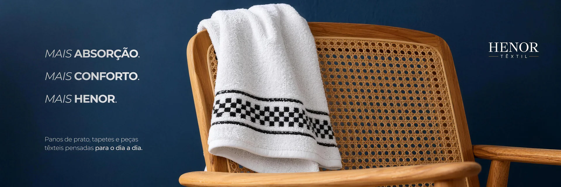 Banner Henor Têxtil: toalha branca com barra xadrez sobre cadeira de palhinha — mais absorção, mais conforto, mais Henor